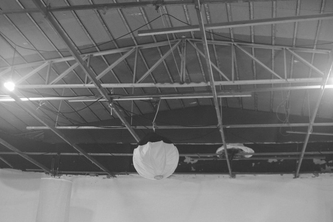 Svartvit bild av ett arenatak med synliga metallbjälkar, kablar och en rund lampa.